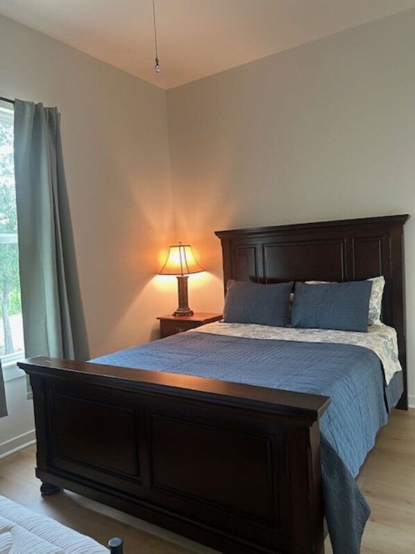 Un dormitorio con una cama de madera oscura, una lámpara de noche y vistas al exterior a través de una ventana con cortinas.