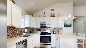 Une cuisine moderne avec des meubles blancs, un lave-vaisselle en acier inoxydable, un four et un revêtement mural en carreaux.
