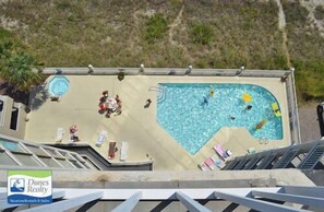 A swimming pool with a unique shape, surrounded by a deck area with lounge chairs and a small circular hot tub.