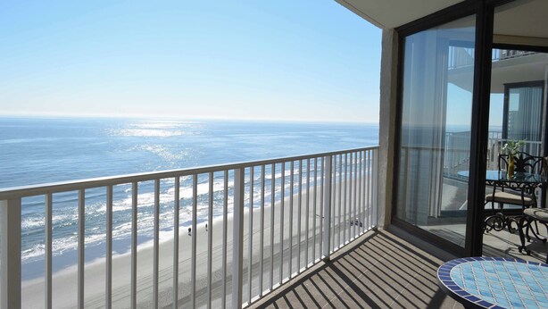 Un balcon avec vue sur l’océan, une porte vitrée et une petite table avec des chaises.