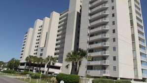Un immeuble résidentiel à plusieurs étages, doté de balcons et entouré de verdure et de palmiers.