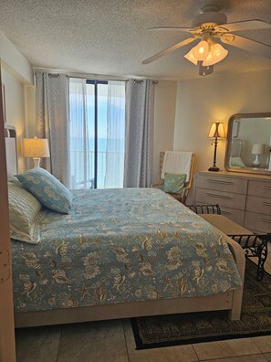 A bedroom with a bed, a ceiling fan, a nightstand, a dresser, and a window with curtains.