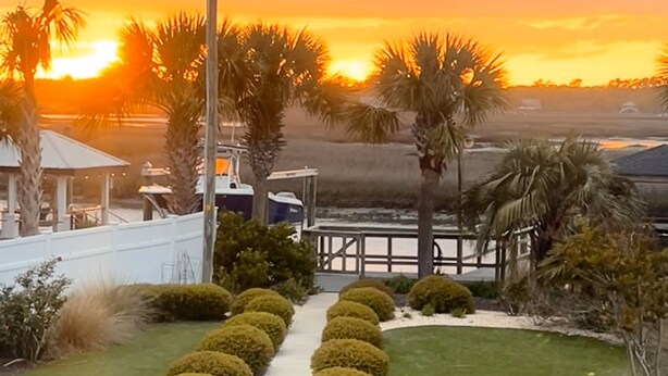 Un jardín ajardinado con un sendero, palmeras y vistas al atardecer.