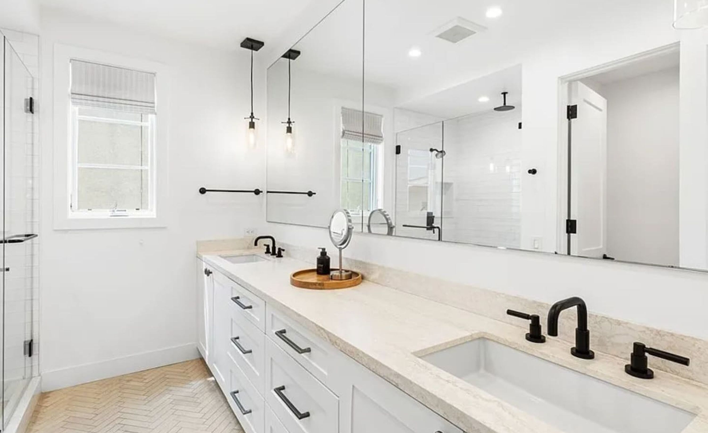 A modern bathroom with a large mirror, two sinks, and a herringbone-patterned floor.