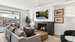 A modern living room with a fireplace, a large TV, and a sofa set. - 3BR Loft Ocean View Rooftop Hot Tub Parking (Newport Beach)