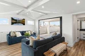 A modern living room with a sofa set, a coffee table, and a bench. There are large windows and a view of the outdoors. - 3BR Loft Ocean View Rooftop Hot Tub Parking (Newport Beach)