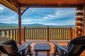 A wooden deck with a view of mountains, two chairs, and a table with glasses on it.