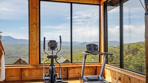 A gym with exercise equipment and large windows offering a mountain view. - Breathtaking Mountain Views • Resort Pool • Hot Tub • Sauna • Near Pigeon Forge (Sevierville)