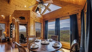 A wooden cabin with a dining area featuring a round table, chairs, and a view of the mountains. - Breathtaking Mountain Views • Resort Pool • Hot Tub • Sauna • Near Pigeon Forge (Sevierville)