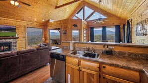 A wooden cabin interior with a kitchen, dining area, and fireplace. - Breathtaking Mountain Views • Resort Pool • Hot Tub • Sauna • Near Pigeon Forge (Sevierville)
