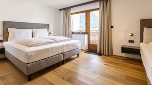 Un dormitorio moderno con una cama grande, suelo de madera, una ventana con cortinas y vistas al balcón.