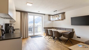 Una cocina moderna con cafetera, un comedor con mesa y sillas, un amplio ventanal con cortinas y un televisor de pantalla plana en la pared.