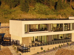 A modern two-story building with large windows, outdoor seating, and a stone facade.
