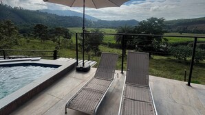 A poolside area with two lounge chairs and an umbrella, overlooking a scenic landscape with hills and a clear sky. - HORIZONTE CHALET - Cozy A-frame chalet in Rio Piracicaba (MG) (Rio Piracicaba)