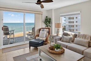 Ein geräumiges Wohnzimmer mit Balkon und Blick auf den Ozean, ausgestattet mit einer bequemen Couch, einem Couchtisch und einem Deckenventilator.
