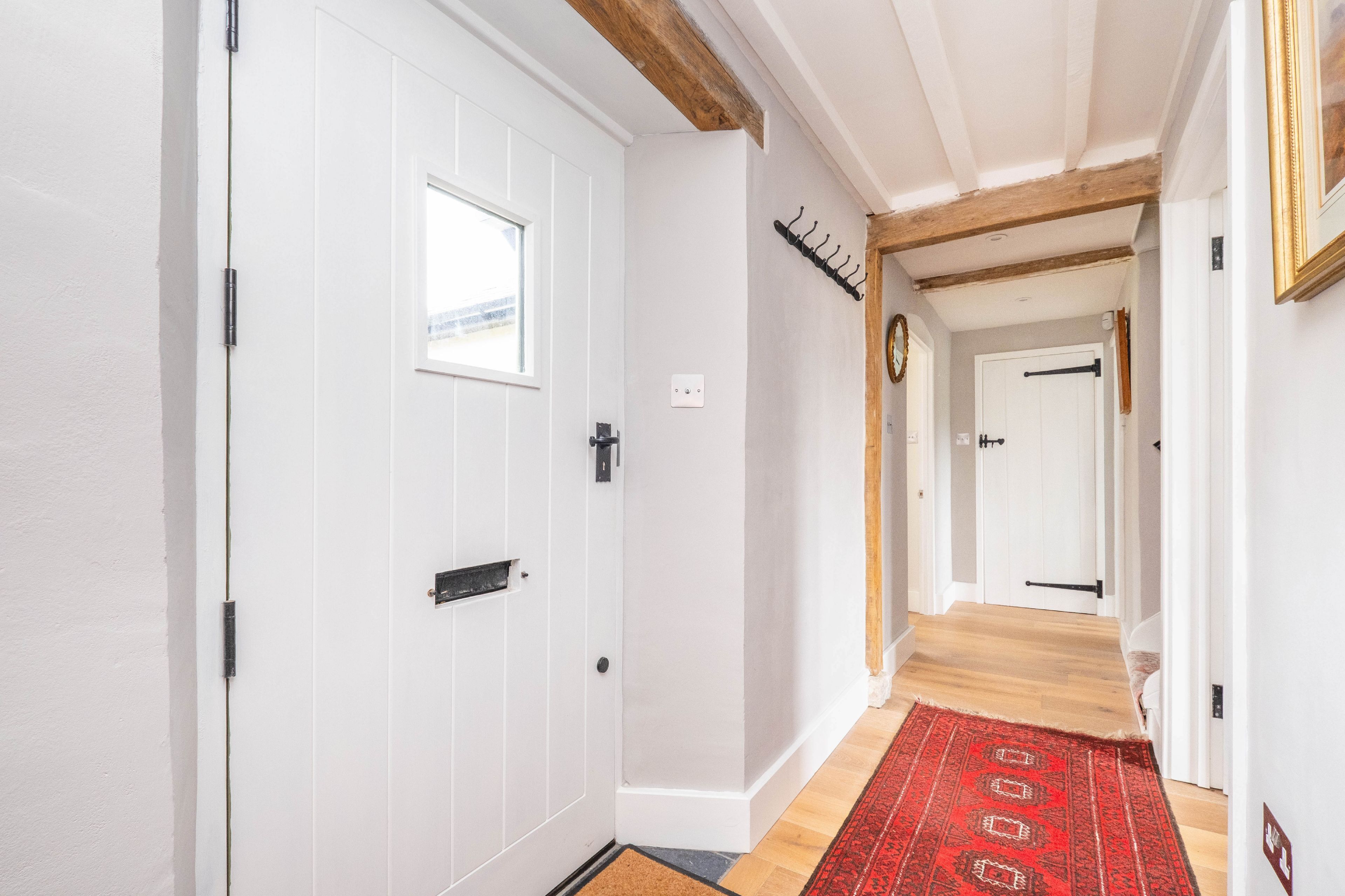 A hallway with white walls, wooden beams, and a red patterned rug.