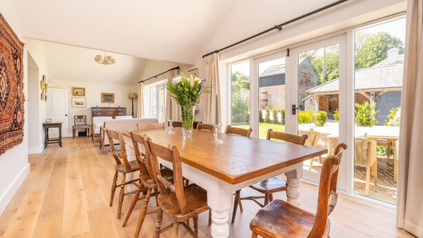 Un espace repas avec une table et des chaises en bois, de grandes fenêtres et une vue sur l’extérieur.
