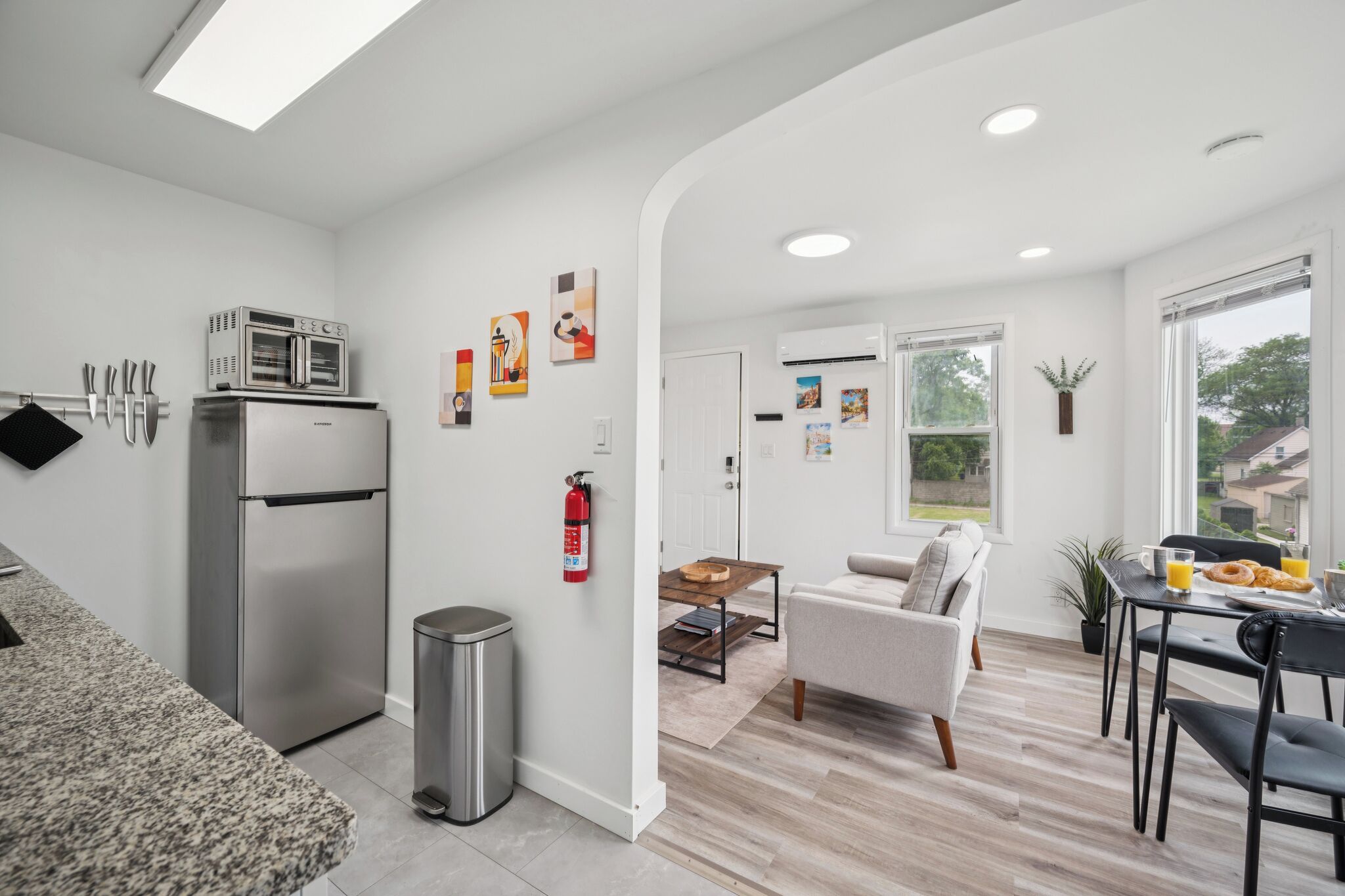 A modern kitchen with a stainless steel refrigerator, a dining area with a table and chairs, and a living space with a sofa and a coffee table.