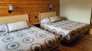 A cabin-style room with two wooden beds, each with a patterned bedspread and matching pillows. There are two wall-mounted lamps on either side of the beds. - Bush Pilot Cabin-Modern Comfort in the Last Frontier (For families or casual travelers) (Tok)