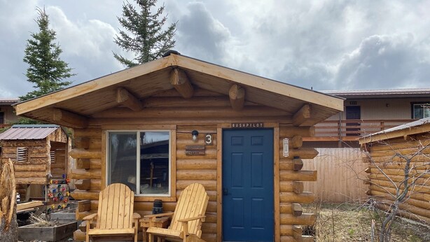 A log cabin with a blue door, two wooden Adirondack chairs, and a small porch area. - Bush Pilot Cabin-Modern Comfort in the Last Frontier (For families or casual travelers) (Tok)