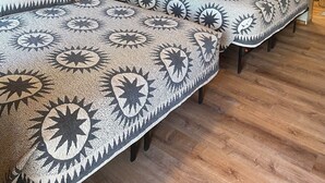 Ein Holzhütten-Zimmer mit zwei Betten, jeweils mit gemusterten Bettdecken, einer Wandlampe und einem gerahmten Bild an der Wand.