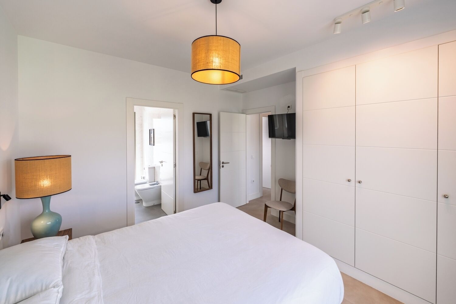 A bedroom with a bed, a lamp, a wardrobe, a mirror, and a television.