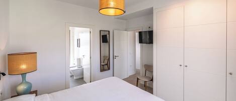 A bedroom with a bed, a lamp, a wardrobe, a mirror, and a television.