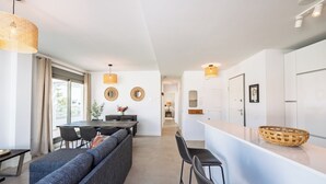 A modern kitchen with white cabinets, a dining area with a long table and chairs, and a seating area with a sofa and chairs.