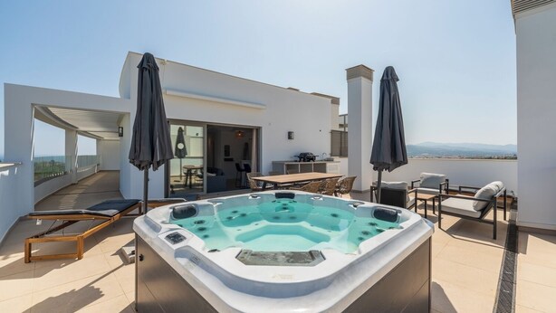 A rooftop terrace with a hot tub, outdoor seating, and a view of the landscape.