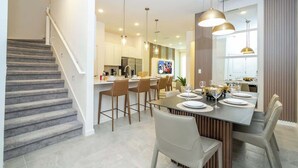Una cocina moderna con comedor, escalera e iluminación colgante.
