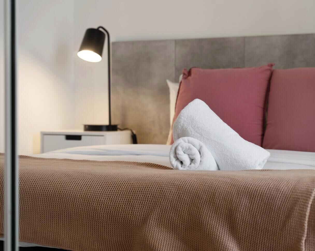 A neatly made bed with a white towel, a brown bedspread, and a headboard with a grey panel.