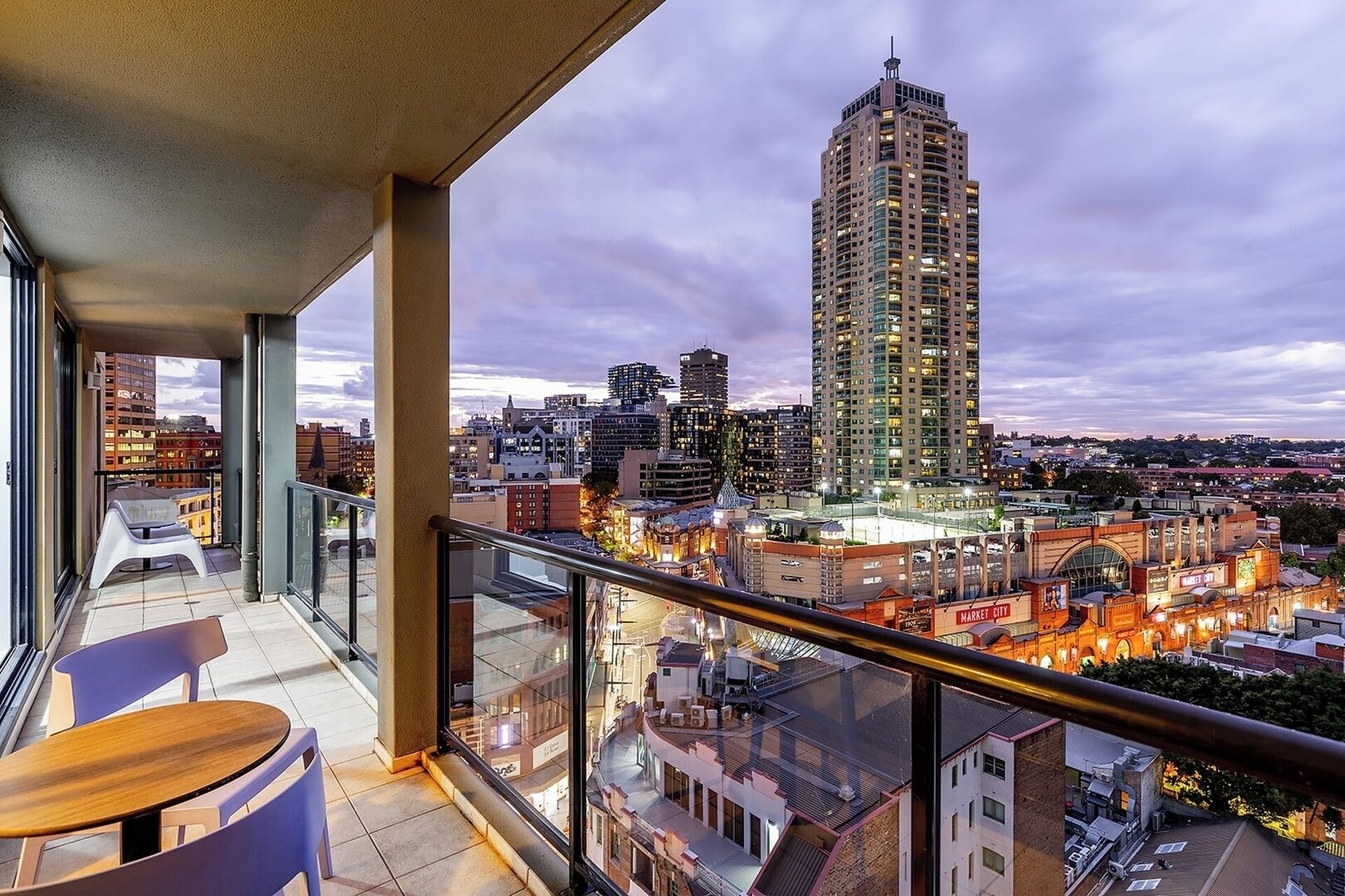 A balcony with a view of a cityscape, including a tall building and a market area.
