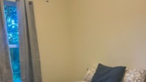 Une chambre à coucher avec un lit, une fenêtre avec des rideaux et une vue sur les arbres à l’extérieur.