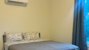 Une chambre à coucher avec un lit, une fenêtre avec des rideaux et un appareil de climatisation fixé au mur.