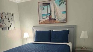 A bedroom with a large bed, a nightstand, a lamp, and a painting of a beach scene. - Sunset paradise, entire rental unit in Tampa,florida (Tampa)