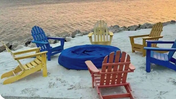 A beach scene with several Adirondack chairs and a blue bean bag chair on the sand near the water. - Sunset paradise, entire rental unit in Tampa,florida (Tampa)