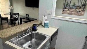 A kitchen with a stainless steel sink, a small dining area with a table and chairs, and a painting on the wall. - Sunset paradise, entire rental unit in Tampa,florida (Tampa)