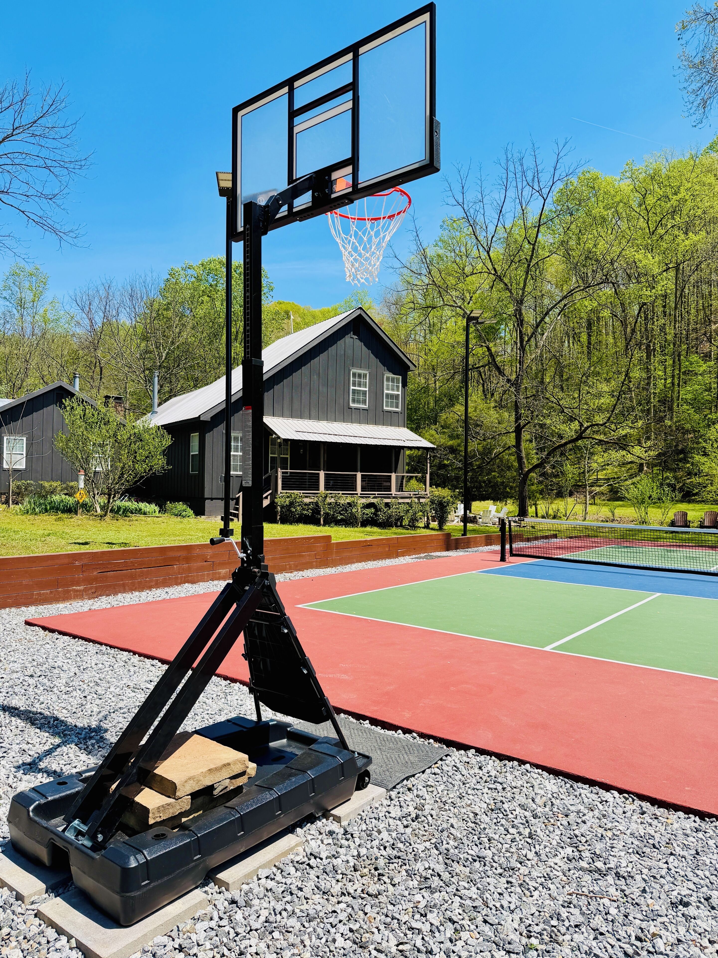 Una cancha de baloncesto con aro y red, rodeada por una zona de grava y una terraza de madera.