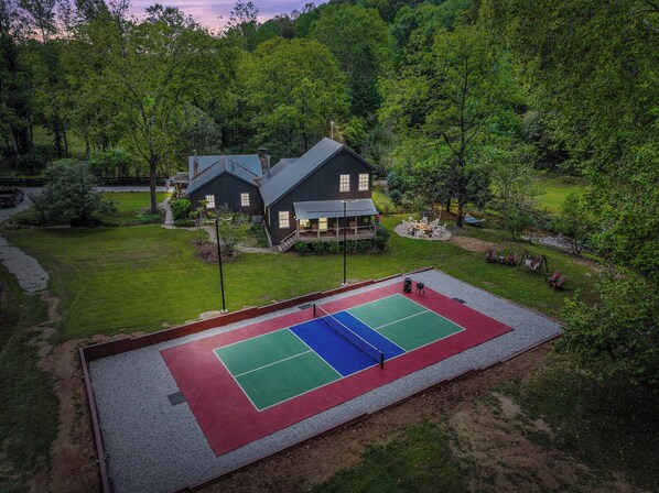 Una casa con cancha de tenis, rodeada de zona boscosa.