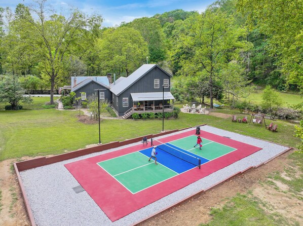 Una cancha de tenis con una red, rodeada de césped y una casa al fondo.