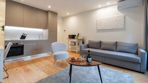 A modern living room with a grey sofa, a white armchair, and a coffee table. There is a kitchen area with a built-in oven and microwave. - Sunny Flats w/ Balcony by HostWise (Guimarães)