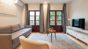 A modern living room with a sofa, a TV, and a small table with a bottle and glasses. - Sunny Flats w/ Balcony by HostWise (Guimarães)
