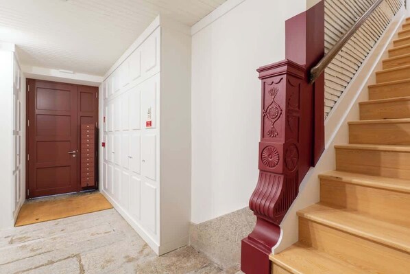 A hallway with a wooden staircase, a red door, and a white door with multiple locks.