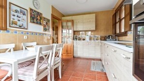 A kitchen with white cabinets, a dining table with chairs, and a tiled backsplash. - Entrencinas - country house in Collera (Ribadesella), Northern Spain (Collera)