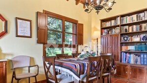 A dining area with a table, chairs, a chandelier, a bookshelf, and a window with curtains. - Entrencinas - country house in Collera (Ribadesella), Northern Spain (Collera)