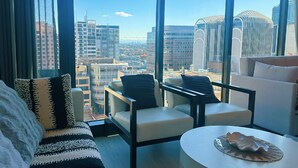 A modern hotel room with a large window offering a city view, a sofa, two armchairs, and a small table with a decorative bowl. - Stylish 1BR suite with City-view & Balcony (Sydney)