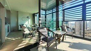 A modern living room with a large glass wall, a dining area with chairs and a table, and a kitchen area with cabinets and a refrigerator. - Stylish 1BR suite with City-view & Balcony (Sydney)