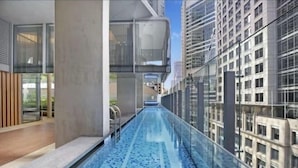 A modern building with a glass-enclosed swimming pool, high-rise buildings in the background, and a clear sky. - Stylish 1BR suite with City-view & Balcony (Sydney)