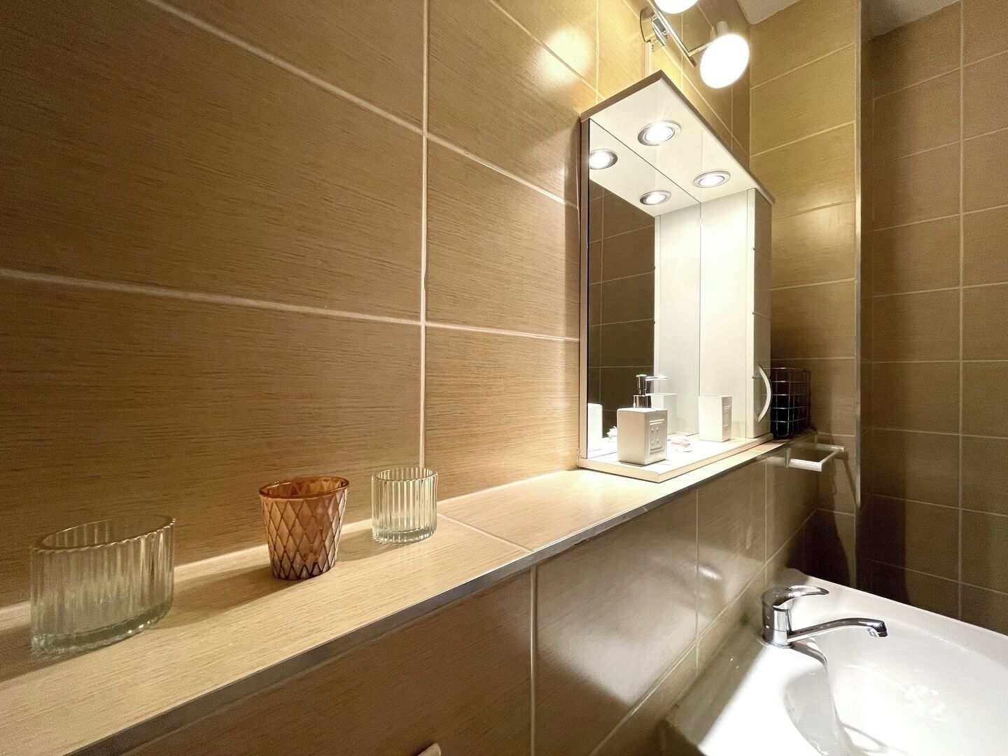 A modern bathroom with a large mirror, a sink, and a vanity with two glass containers.
