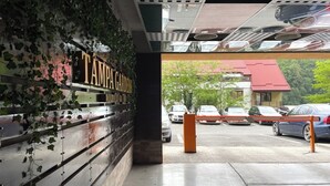 Uma área de estacionamento com uma placa indicando 'TAMPA GARDENS' e vista para carros estacionados e um edifício com telhado vermelho.